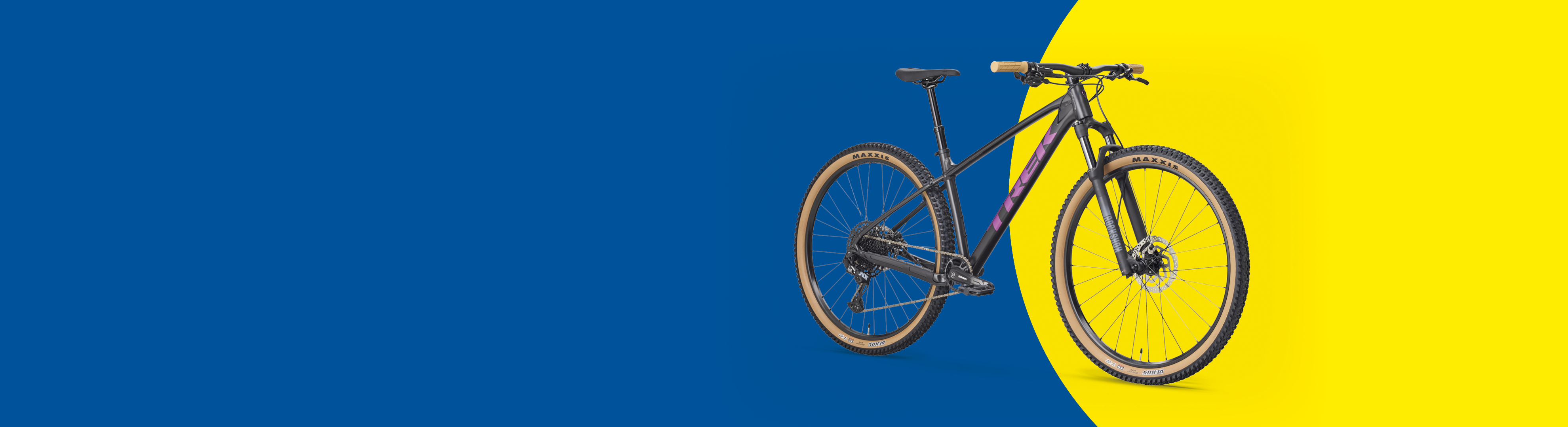 Планински велосипед с черно-лилава рамка и бежови гуми на син и жълт фон.