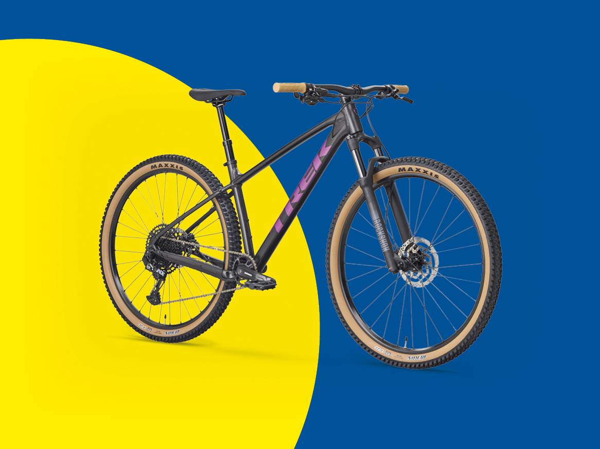 Планински велосипед с черно-лилава рамка и бежови гуми на жълто-син фон.