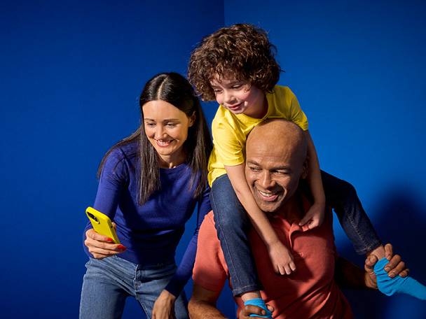 Щастливо семейство се забавлява, докато майката снима с жълт телефон.