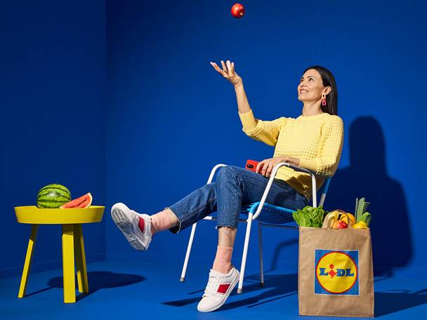 Жена седи на стол, хвърля ябълка във въздуха, докато пазарува в Lidl.