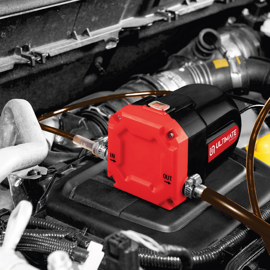 Червена и черна помпа за източване на масло, свързана с маркучи в двигател на автомобил.