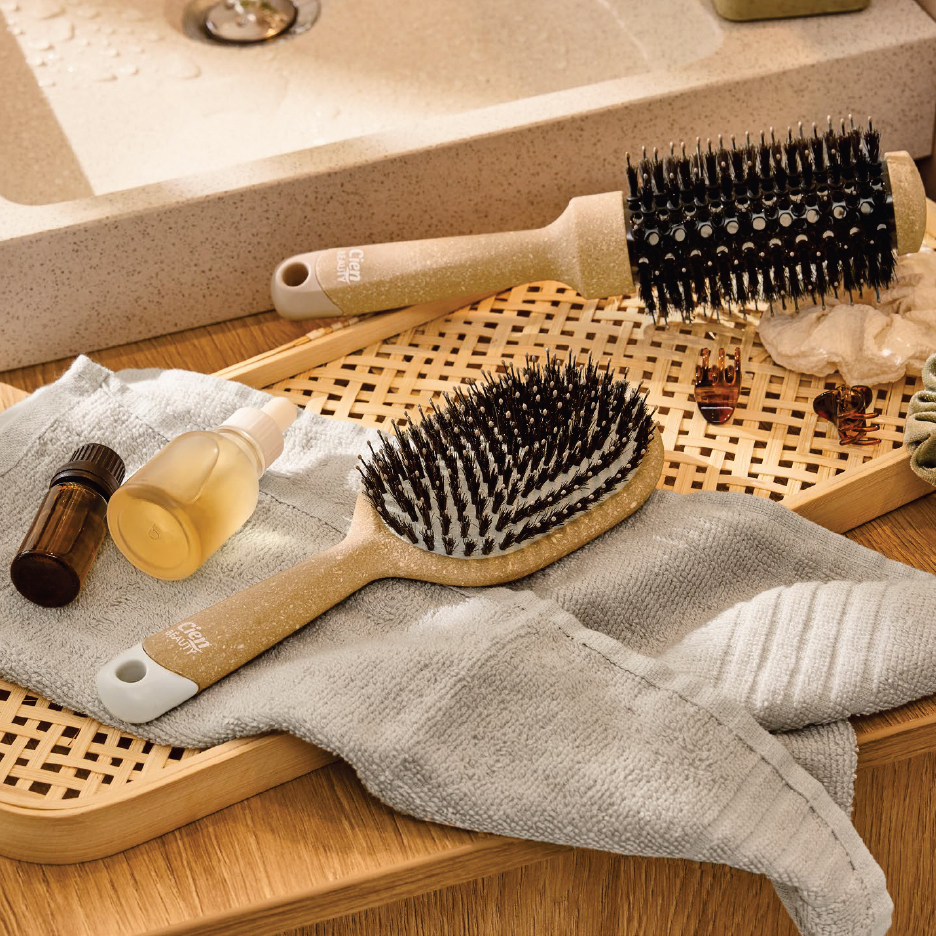 Две четки за коса, етерични масла и кърпа за баня върху дървена табла до мивка.