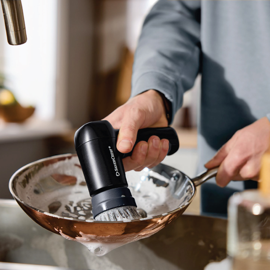 Мъж мие тиган с електрическа четка за почистване в кухнята.