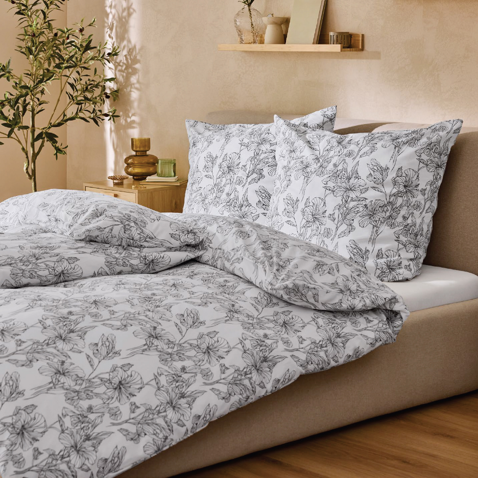 Спално бельо с черно-бял флорален принт в спалня с нощно шкафче и рафт.