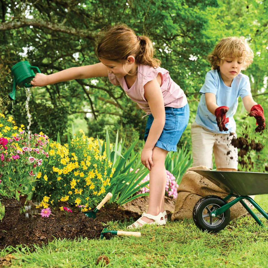 Две деца поливат и копаят в градината с градински инструменти и количка.