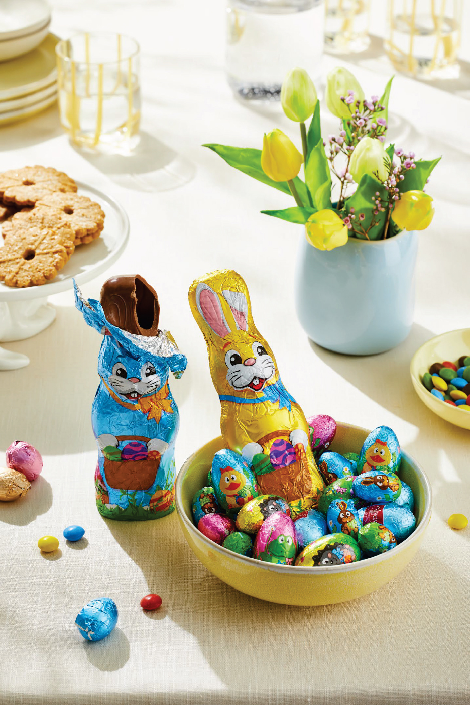 Великденски шоколадови зайци и яйца, бисквити и лалета на маса.