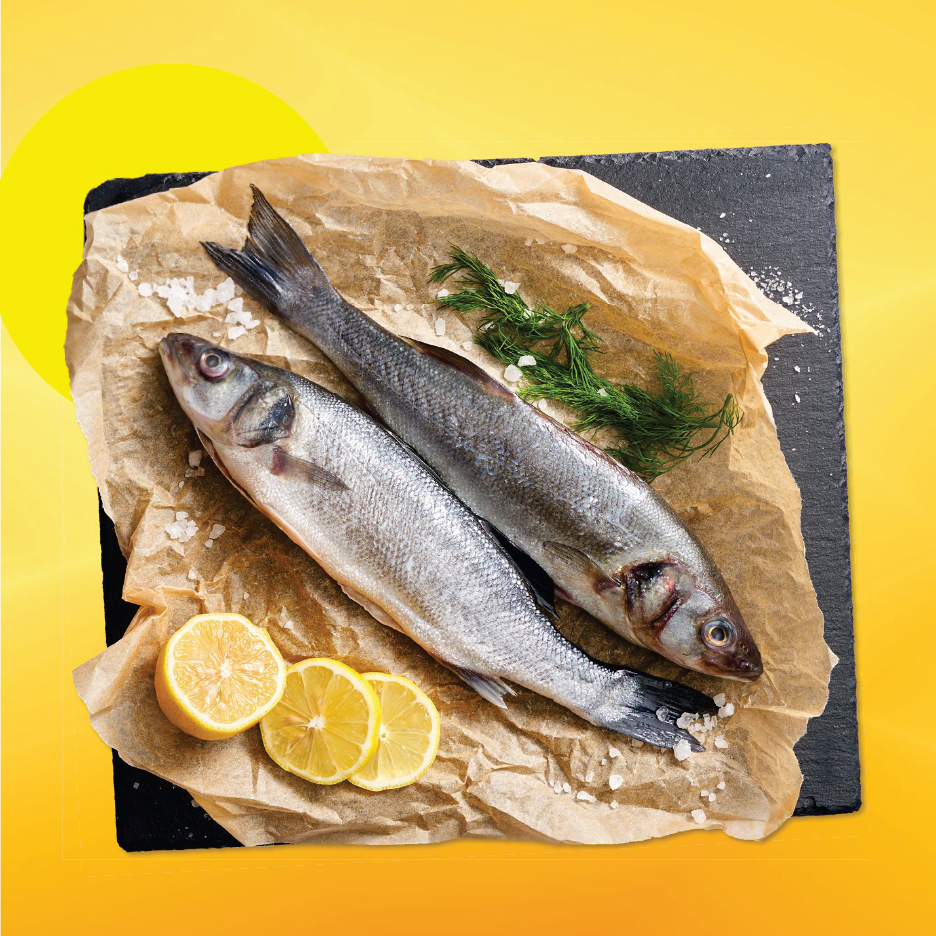 Две сурови риби, лимони и копър върху хартия за печене на черен поднос.