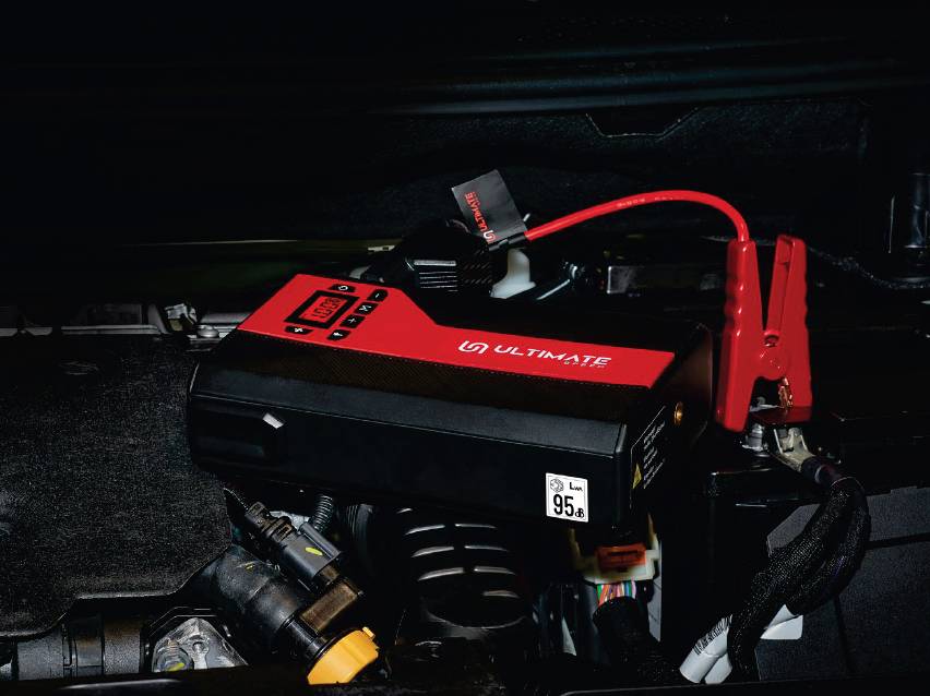 Черно-червен стартов бустер, свързан към акумулатор на кола.