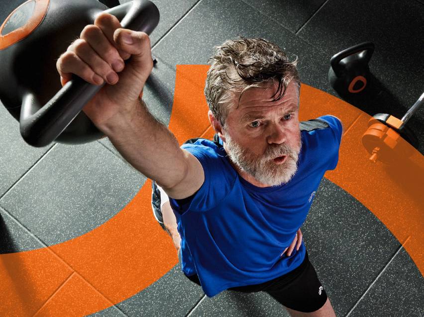 Мъж в синя тениска вдига пудовка във фитнес зала.