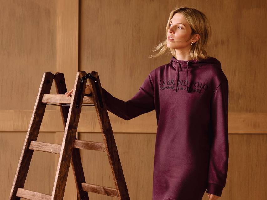 Жена в дълъг суичър с качулка, облегната на дървена стълба.