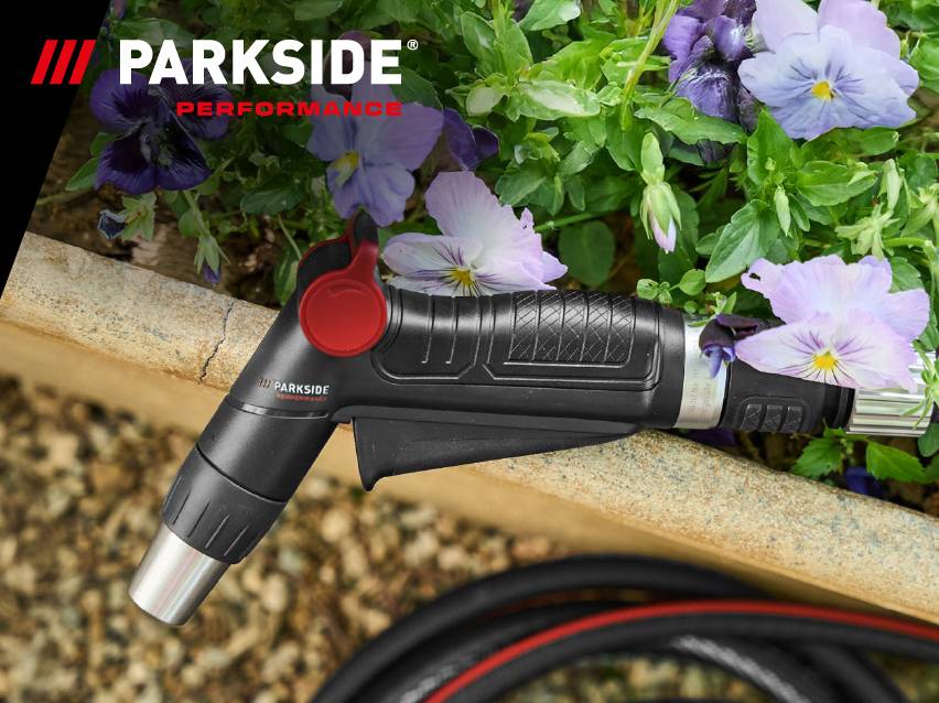 Черен пистолет за поливане с червен спусък, маркуч и виолетови цветя на заден план.