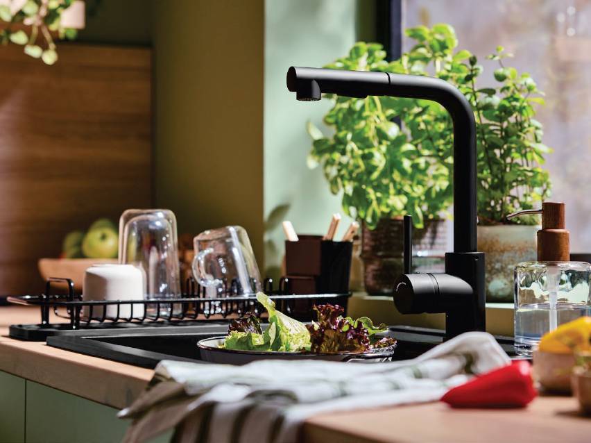 Кухненска мивка с черен кран, сушилник за съдове и свежа салата.