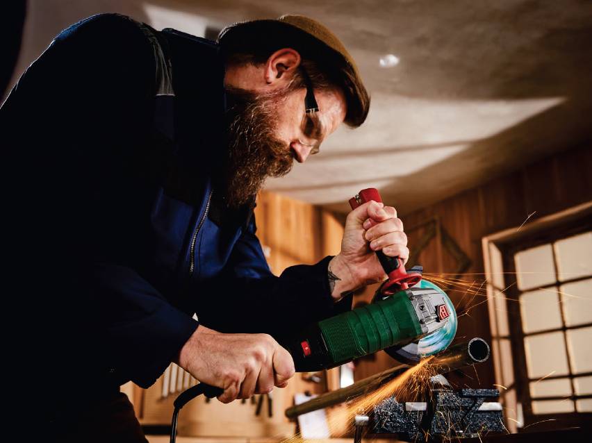 Мъж с ъглошлайф реже метална тръба, създавайки искри.