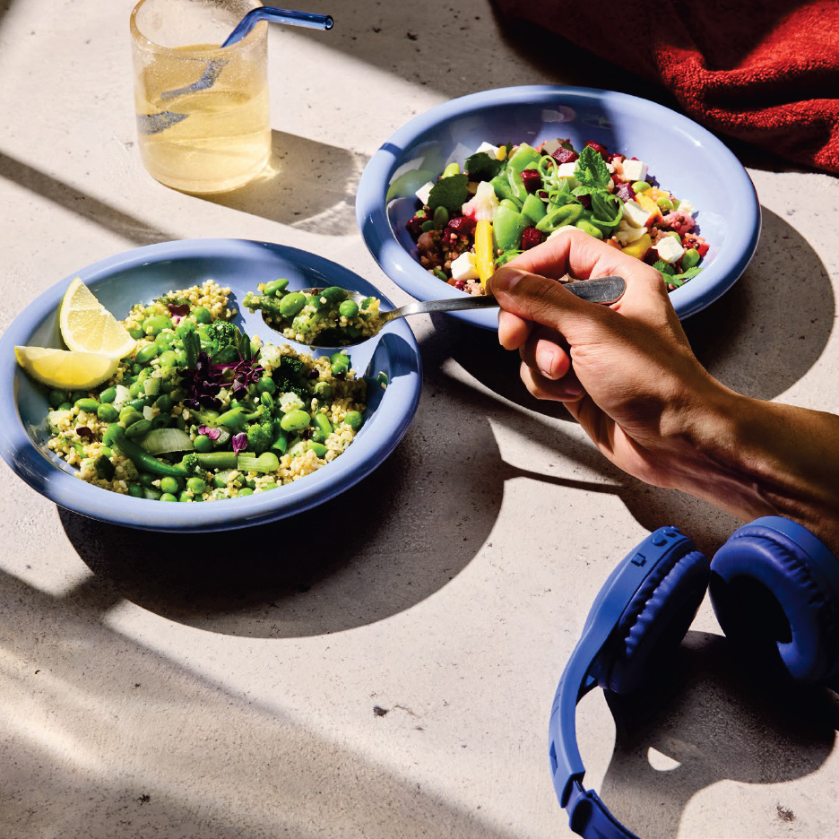 Две купи със салата от киноа и зеленчуци, едната се яде с лъжица, до нея слушалки.