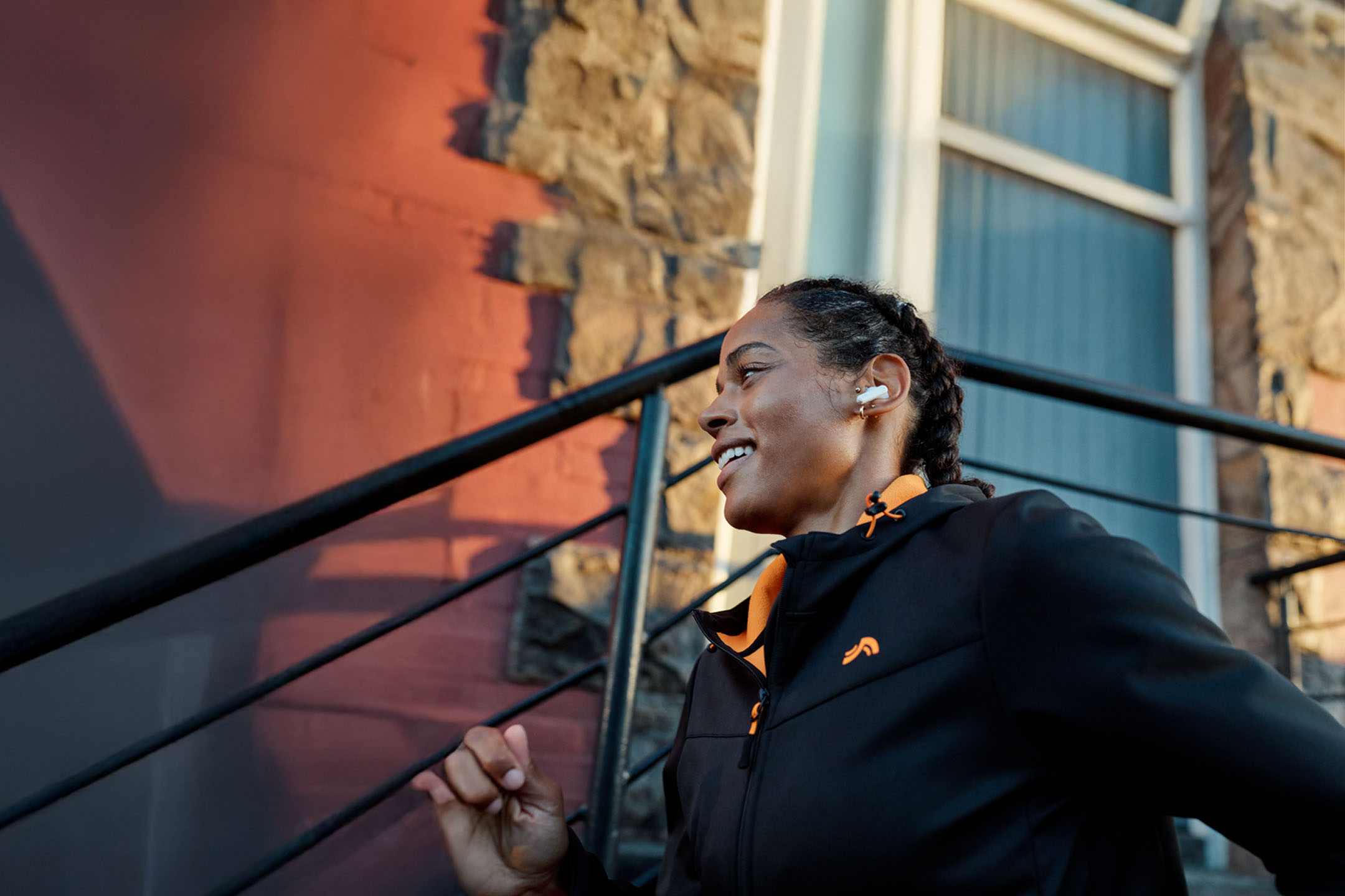 Жена тича с безжични слушалки, облечена в яке.