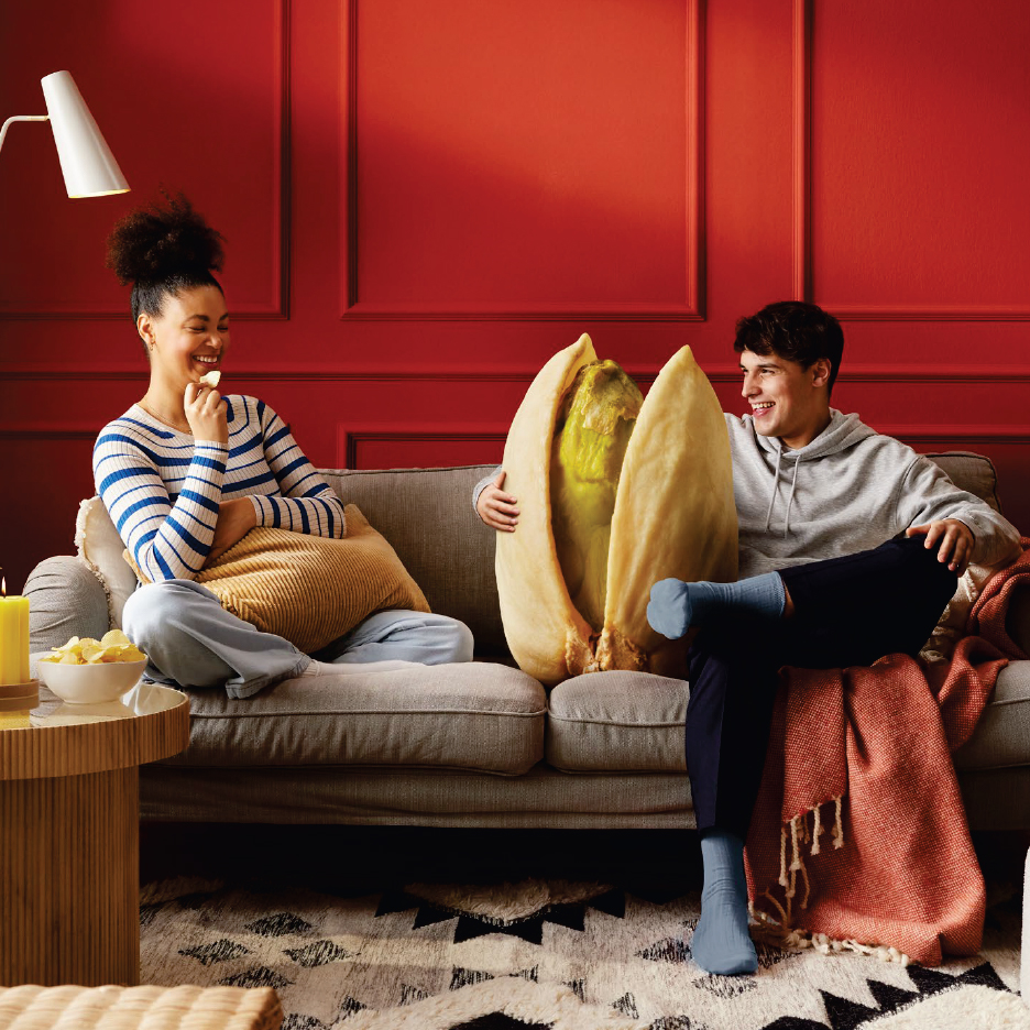 Млада двойка седи на диван с гигантски шамфъстък, наслаждавайки се на закуски.